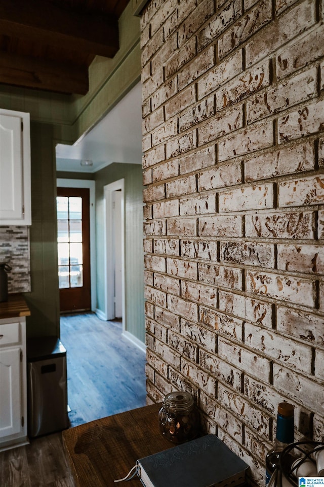 kitchen with wood-type flooring, brick wall, and white cabinets