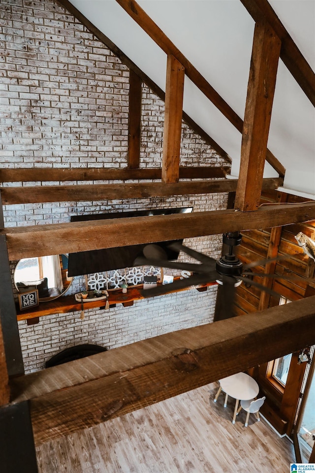 interior space featuring lofted ceiling with beams, brick wall, and hardwood / wood-style flooring