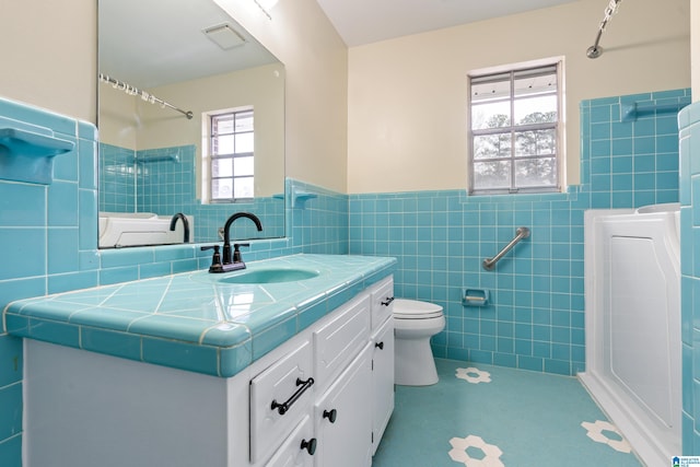 full bath with wainscoting, toilet, walk in shower, vanity, and tile walls