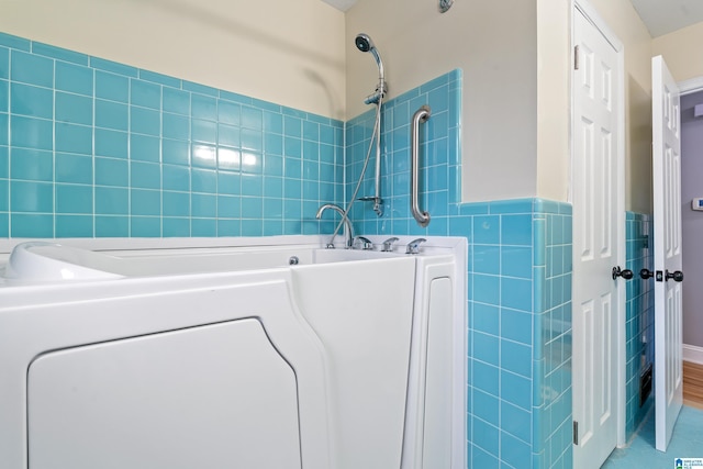 full bathroom with a wainscoted wall, washer / dryer, a garden tub, and tile walls