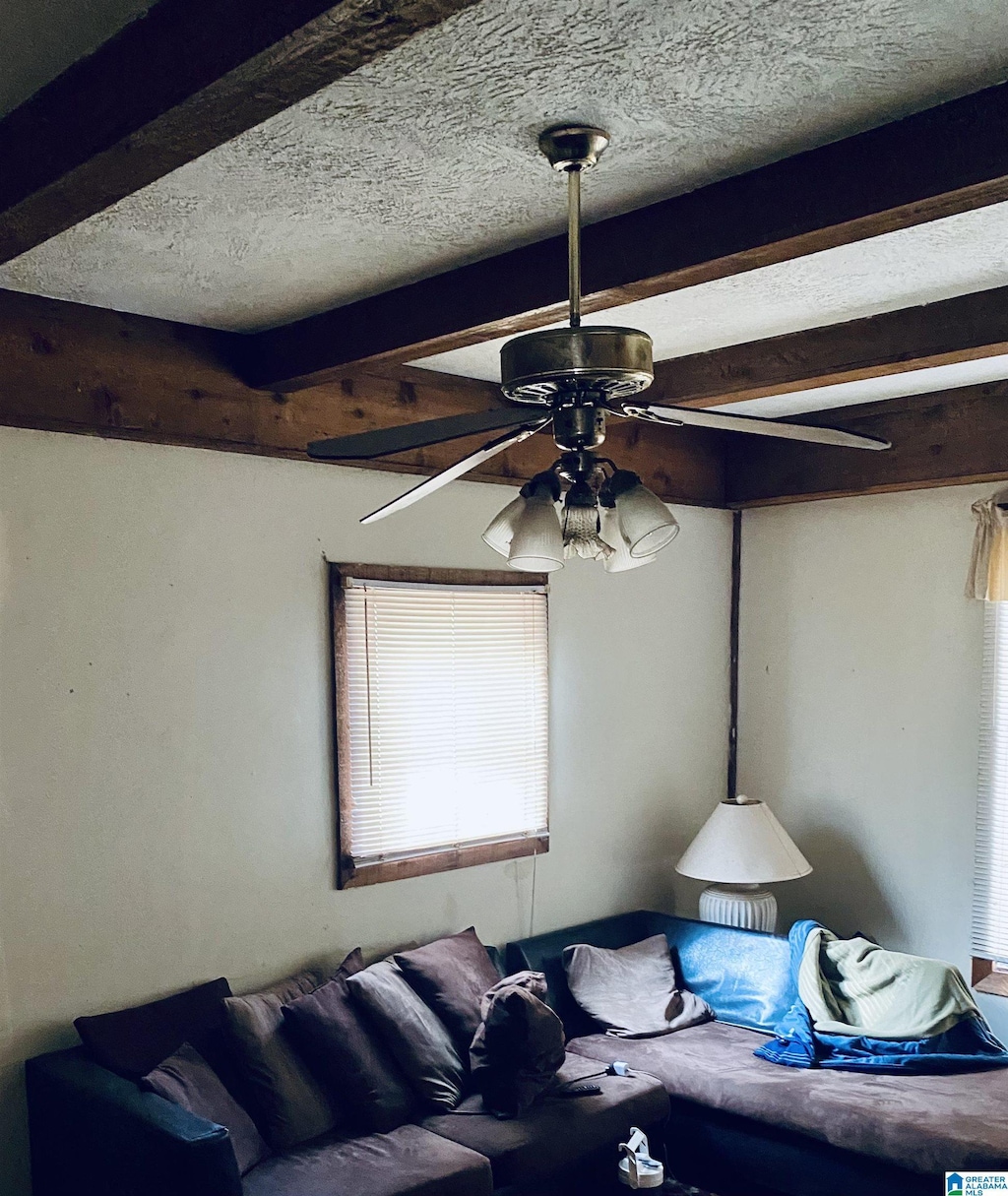 living room with beamed ceiling, ceiling fan, and a textured ceiling