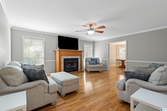 living room with crown molding, ceiling fan, a tile fireplace, and light wood-type flooring