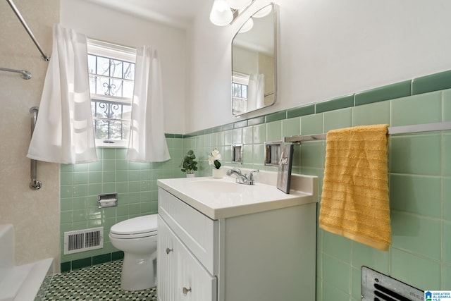 bathroom with vanity, a shower, tile walls, and toilet