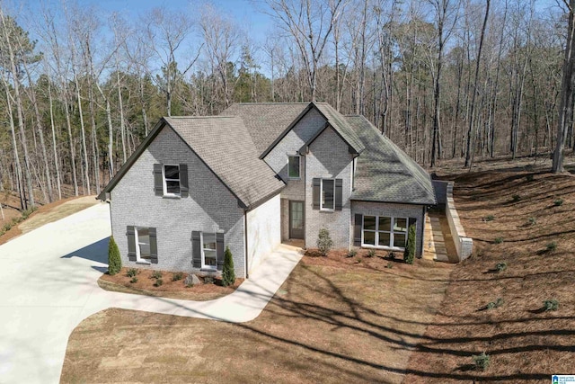 view of front of property featuring brick siding, a shingled roof, a front yard, a wooded view, and driveway