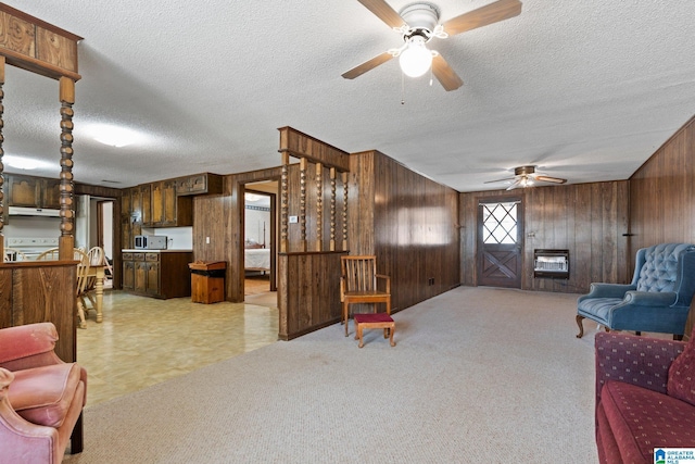 carpeted living room with heating unit, a fireplace, wood walls, ceiling fan, and a textured ceiling