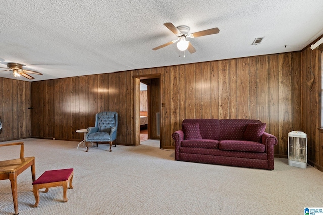 carpeted living room featuring ceiling fan, wooden walls, and a textured ceiling