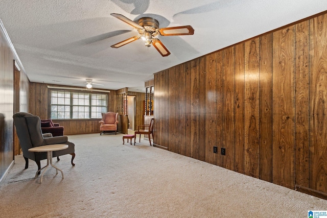 living area featuring ceiling fan, light colored carpet, a textured ceiling, and wooden walls