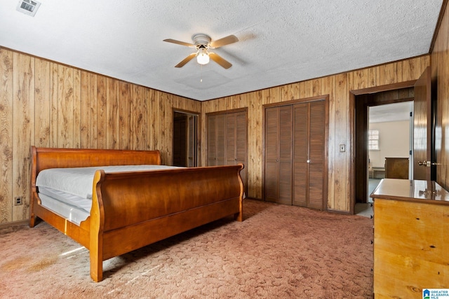 carpeted bedroom featuring ceiling fan, a textured ceiling, multiple closets, and wood walls