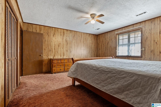 carpeted bedroom featuring ceiling fan, wooden walls, a closet, and a textured ceiling