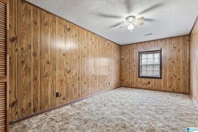 carpeted spare room featuring ceiling fan, a textured ceiling, and wood walls