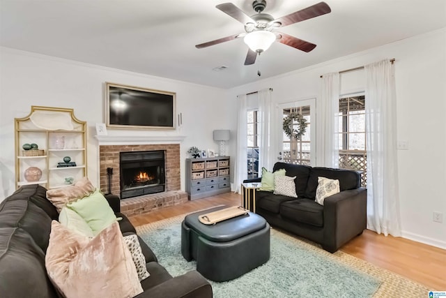 living room with crown molding, ceiling fan, a fireplace, and light hardwood / wood-style flooring