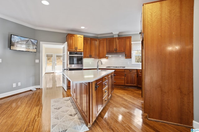 kitchen featuring tasteful backsplash, sink, crown molding, a center island with sink, and light hardwood / wood-style flooring