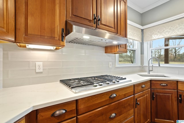 kitchen featuring stainless steel gas stovetop, tasteful backsplash, sink, ornamental molding, and light stone counters