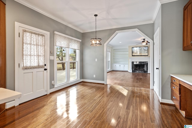 unfurnished dining area with crown molding, ceiling fan, wood-type flooring, and a fireplace