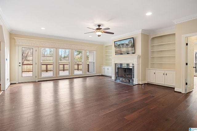 unfurnished living room with crown molding, dark wood-type flooring, built in features, ceiling fan, and a fireplace