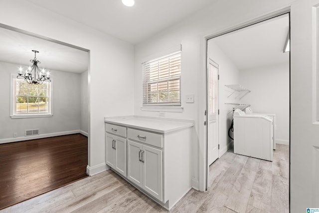 clothes washing area with independent washer and dryer, a chandelier, and light hardwood / wood-style floors