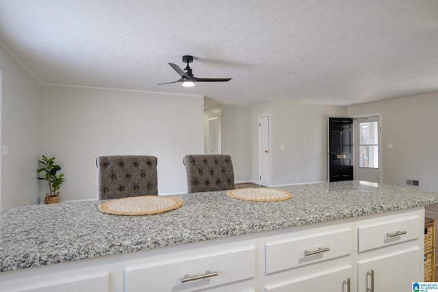 kitchen featuring white cabinetry, ceiling fan, and light stone countertops