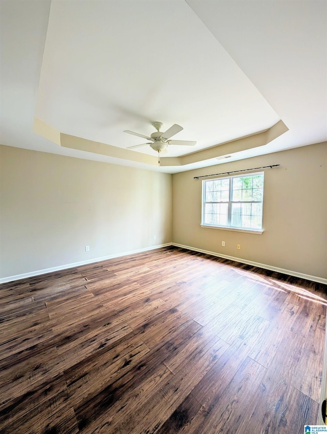 unfurnished room featuring baseboards, a tray ceiling, ceiling fan, and wood finished floors