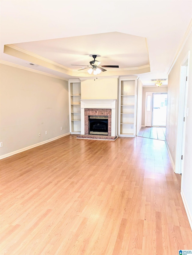 unfurnished living room with a tray ceiling, crown molding, light wood-style flooring, a ceiling fan, and baseboards