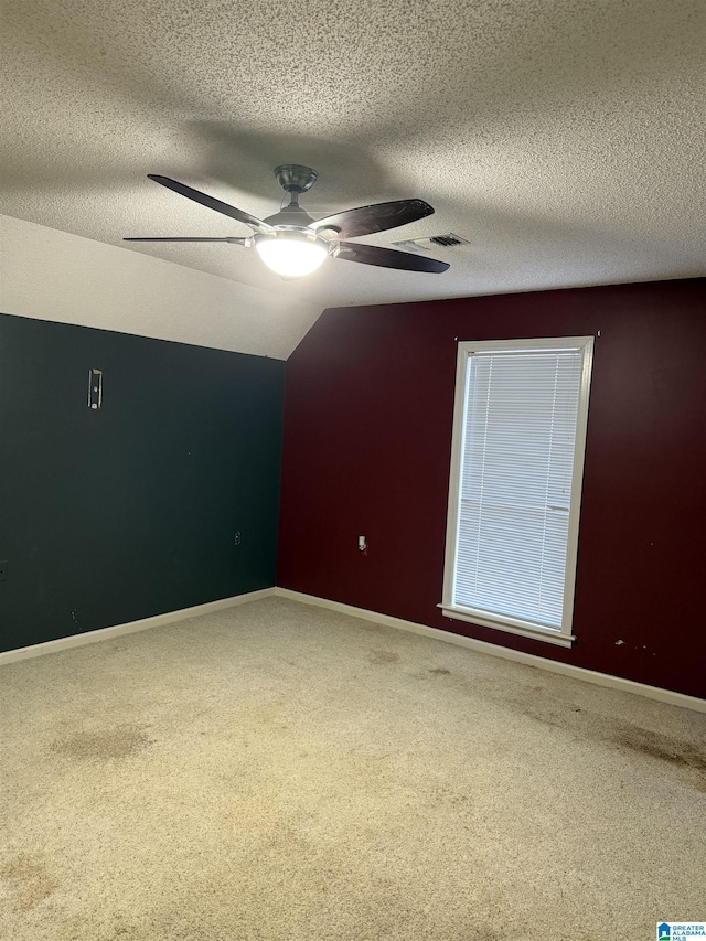 carpeted spare room with a textured ceiling, vaulted ceiling, and ceiling fan