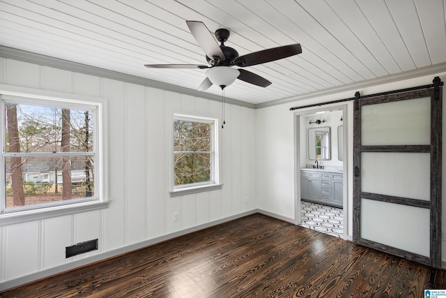 unfurnished bedroom with dark wood-type flooring, ceiling fan, ensuite bathroom, ornamental molding, and a barn door