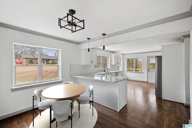 kitchen with sink, white cabinetry, decorative light fixtures, kitchen peninsula, and backsplash