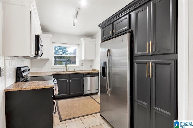 kitchen with light tile patterned floors, a sink, white cabinets, appliances with stainless steel finishes, and decorative backsplash