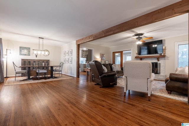 living room with dark hardwood / wood-style flooring, a brick fireplace, ceiling fan with notable chandelier, and a healthy amount of sunlight