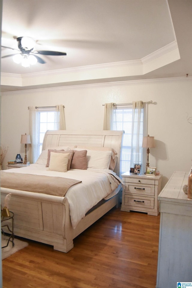 bedroom with crown molding, dark wood-type flooring, ceiling fan, and a tray ceiling