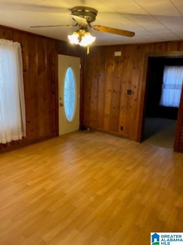 interior space with wooden walls, ceiling fan, and light hardwood / wood-style flooring