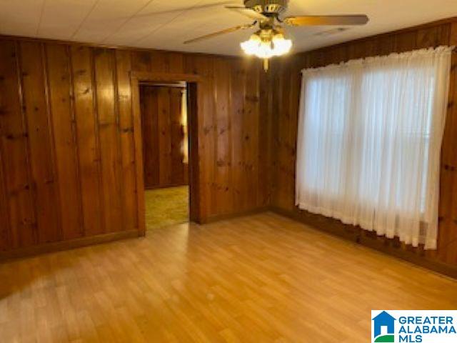 unfurnished room featuring ceiling fan, light hardwood / wood-style floors, and wooden walls