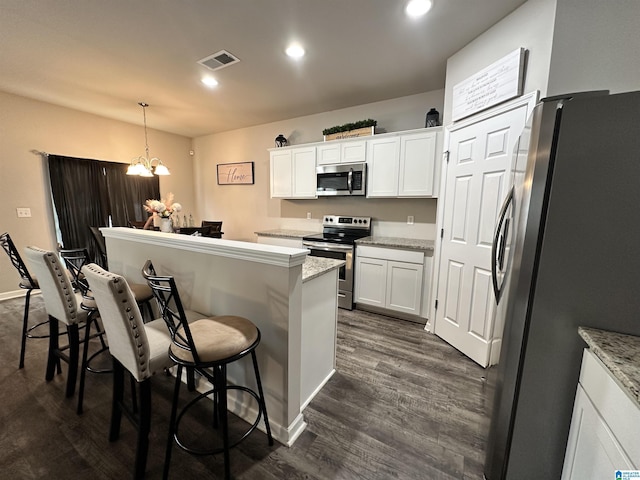 kitchen featuring decorative light fixtures, a kitchen breakfast bar, stainless steel appliances, light stone countertops, and white cabinets