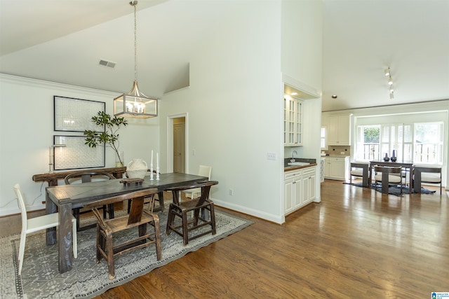 dining room featuring dark wood-type flooring, sink, a notable chandelier, and high vaulted ceiling