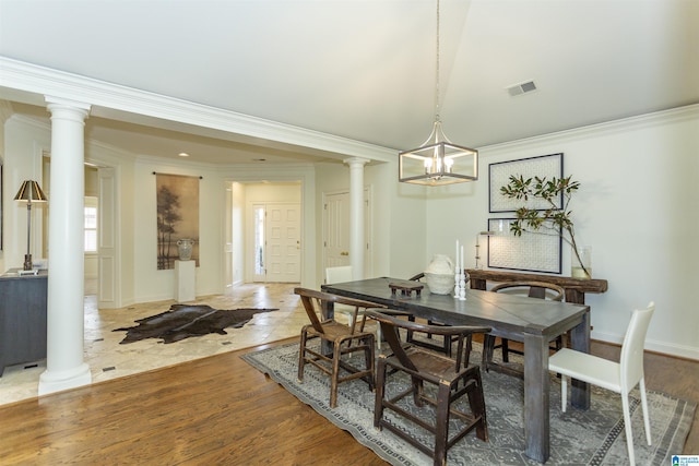 dining area featuring crown molding, a notable chandelier, wood-type flooring, and ornate columns