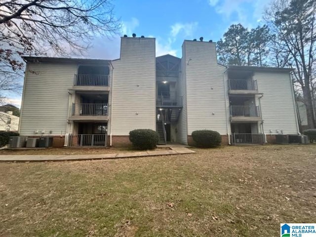 rear view of house with central AC unit and a lawn