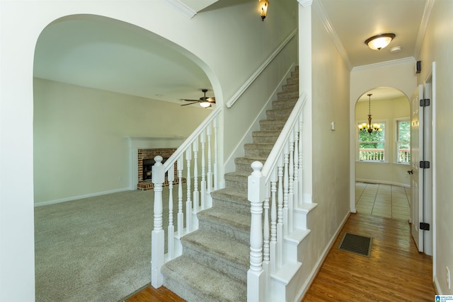 stairway featuring hardwood / wood-style floors, ceiling fan with notable chandelier, a fireplace, and ornamental molding