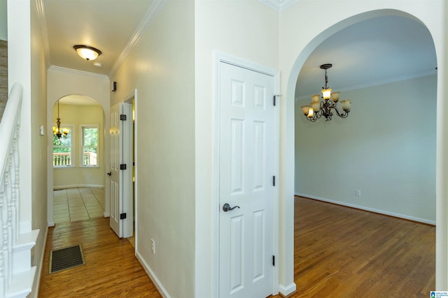 hall with hardwood / wood-style flooring, crown molding, and an inviting chandelier