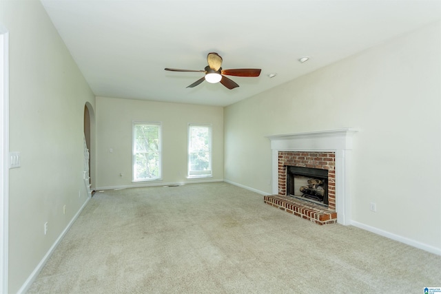 unfurnished living room with light carpet, a brick fireplace, and ceiling fan