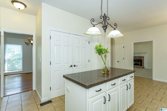 kitchen with light tile patterned flooring, white cabinetry, hanging light fixtures, a kitchen island, and a fireplace