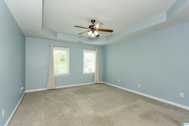 spare room with a raised ceiling, light colored carpet, and ceiling fan