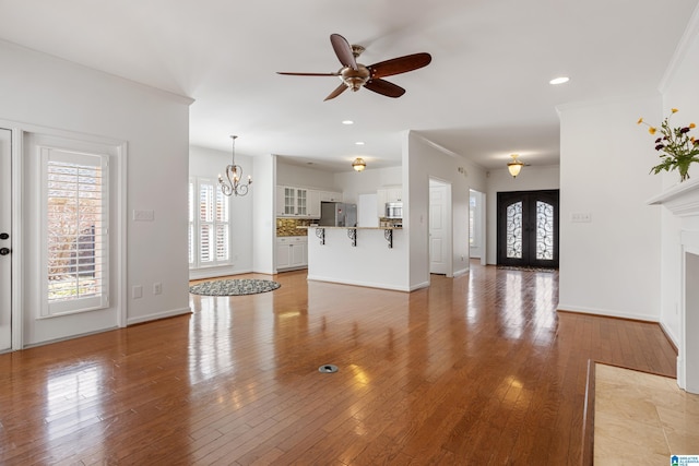 unfurnished living room with crown molding, wood-type flooring, french doors, and ceiling fan with notable chandelier