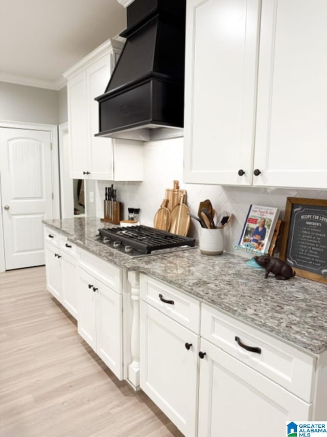 kitchen featuring light stone counters, ornamental molding, custom range hood, white cabinets, and stainless steel gas stovetop