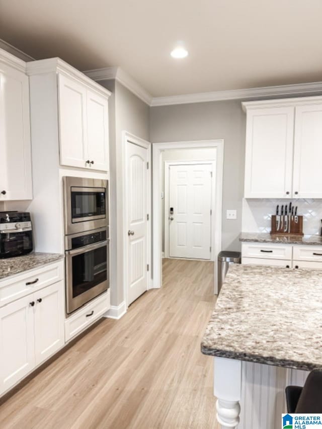 kitchen with stainless steel appliances, white cabinetry, light stone countertops, and crown molding