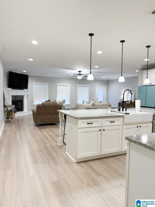 kitchen with white cabinetry, fridge, a center island with sink, decorative light fixtures, and light wood-type flooring