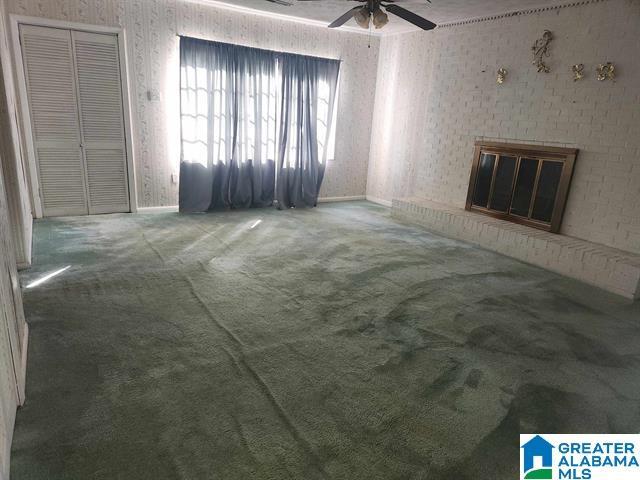 carpeted empty room featuring a brick fireplace and ceiling fan