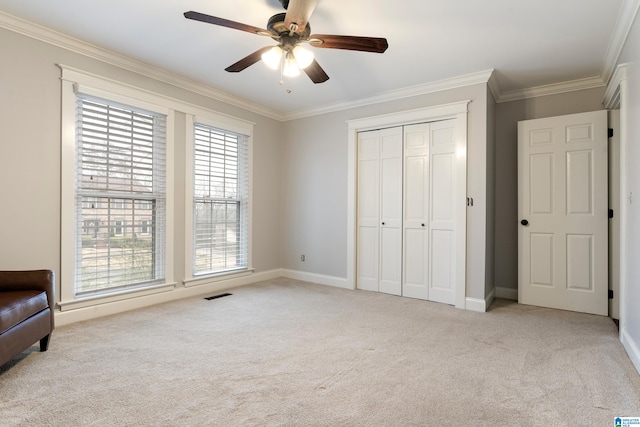 unfurnished bedroom with crown molding, light colored carpet, a closet, and ceiling fan