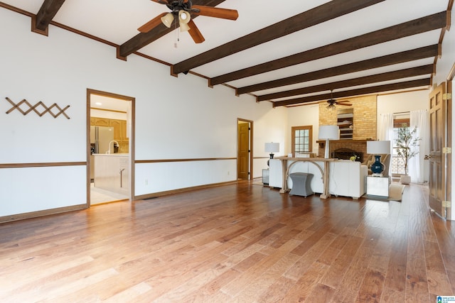 living room featuring beamed ceiling, ceiling fan, a brick fireplace, and light hardwood / wood-style flooring