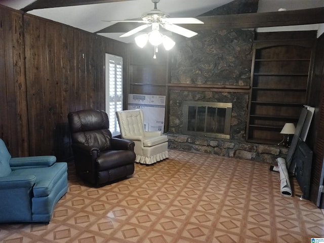 living room with ceiling fan, wooden walls, a stone fireplace, and built in features