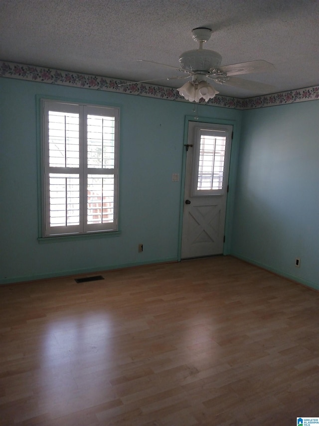 spare room featuring a textured ceiling, ceiling fan, light wood-type flooring, and a wealth of natural light