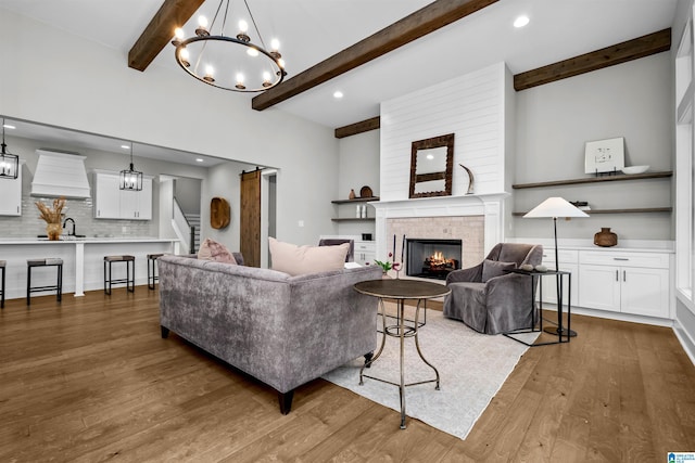 living room with sink, hardwood / wood-style floors, a brick fireplace, a barn door, and beamed ceiling